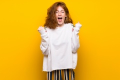 Young redhead woman over yellow wall happy and jumping