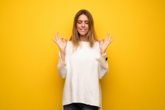 Blonde woman over yellow wall in zen pose