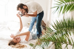 Cheerful young couple taking photos indoors while laying on bed