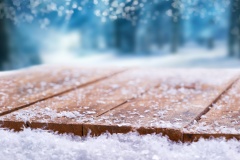 Wooden table top covered in snow with a Christmass, winter and snowy background with space to add products and text.