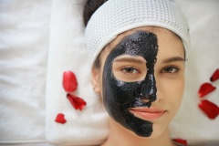 Beautiful young woman relaxing with face mask at beauty spa. Woman getting facial black mud mask at beauty salon.