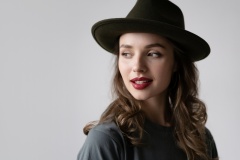 Close up portrait of  female in stylish black hat with brown curls and wine red lips posing in studio isolated on gray background. Autumn fashion concept.