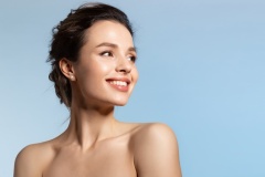 Toothy smiling young woman with shiny glowing perfect facial skin and bare shoulder looking aside.