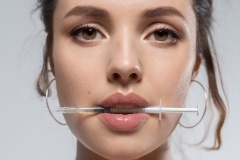 Young beautiful woman face with syringe in mouth portrait.