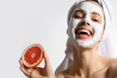 Close up of funny  girl in towel with natural mask on face holding orange and grapefruit isolated on white studio background. Trendy advertising poster of organic fruit skincare mask.
