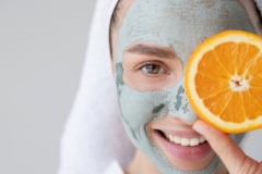 Closeup woman face with clay mask and orange fruit slice.