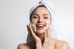 Happy laughing  woman  in head towel washing face with foam soap cosmetic product.