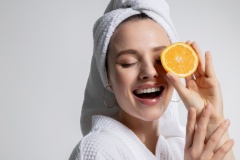 Smiling happy young beautiful girl in bathrobe and head towel holding orange citrus fruit round slice.