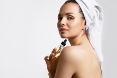 Close up of beautiful young woman in towel showing moisturizing facial serum