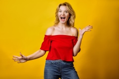 young blond woman laughing, smilling, dressed in red top posing isolated on yellow background in studio. People lifestyle concept. Mock up copy space. Having fun, fooling around with fluttering hair